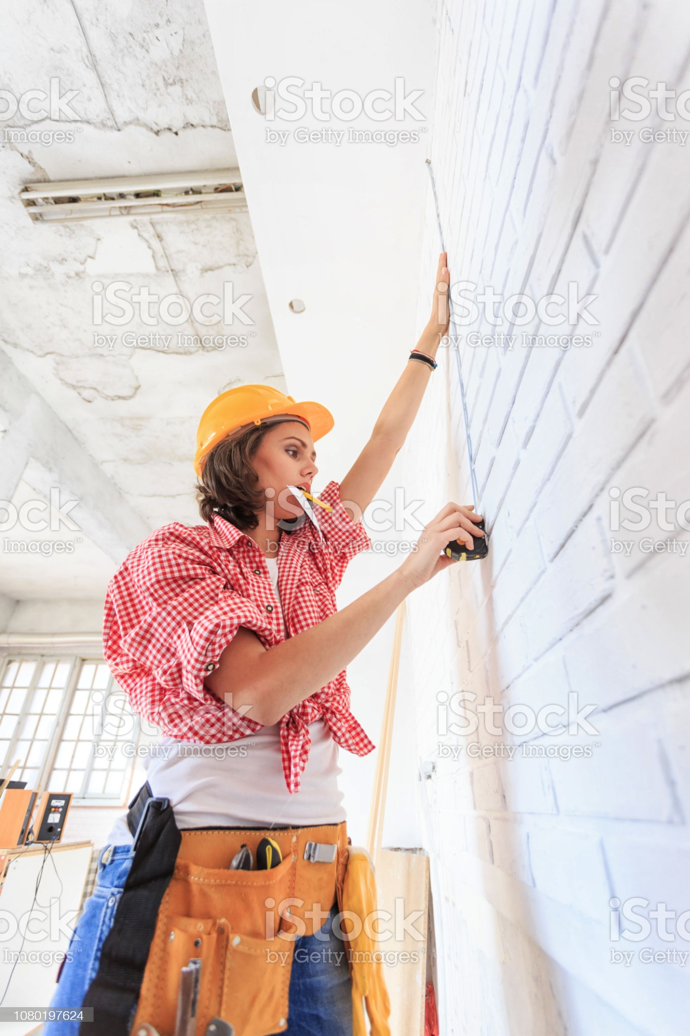Female worker with tool belt and helmet using tape meausre.